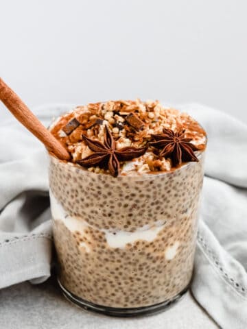 This is a photo of the pumpkin spice chia pudding in a cup layered with yogurt in between and topped with granola, star anise and a stick of cinnamon (to make it pretty).