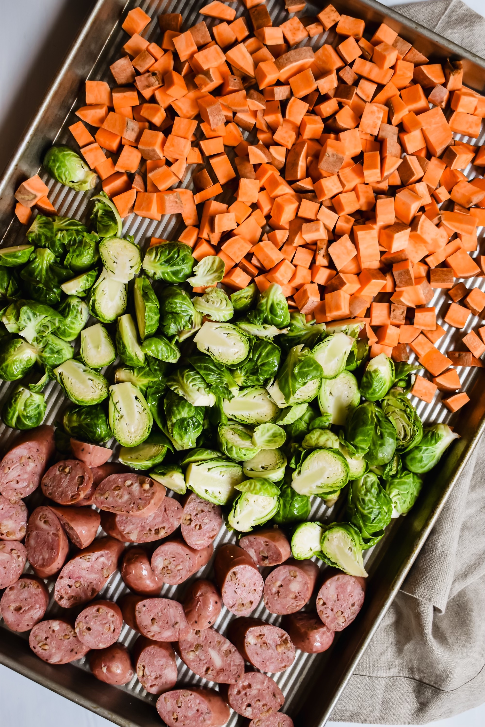 This is a top view of the sweet potatoes, brussels sprouts and chicken apple sausage on a sheet pan, ready to bake.