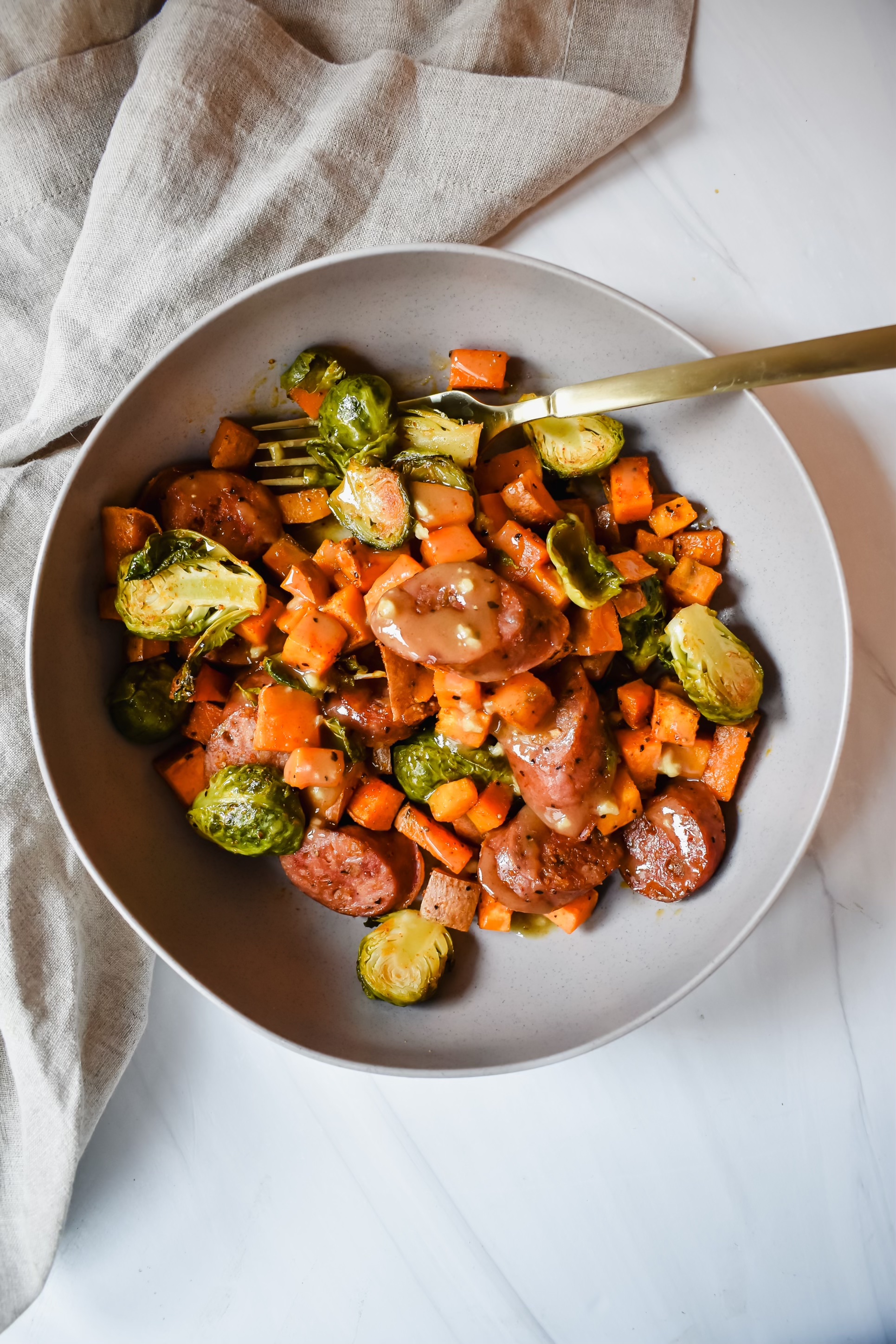 This is a top view of my chicken apple sausage sheet pan dinner featuring brussles sprouts, sweet potatoes and apple sausage with a honey dijon dressing drizzled on top.